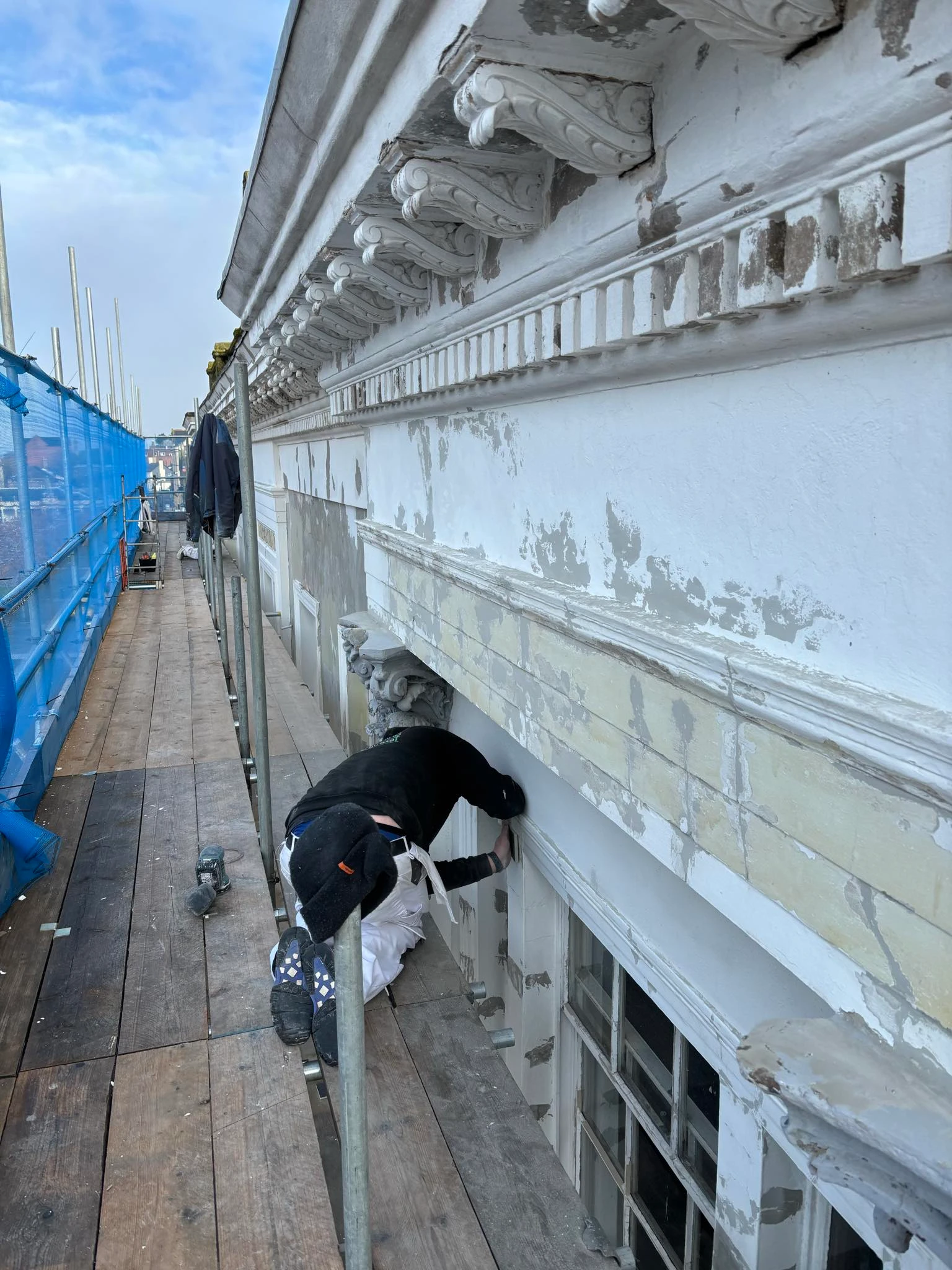 Painter working on ornate cornice details of Bridge Buildings from scaffolding