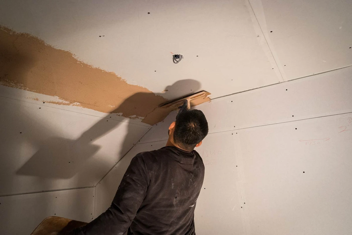 Professional plasterer applying plaster to ceiling drywall