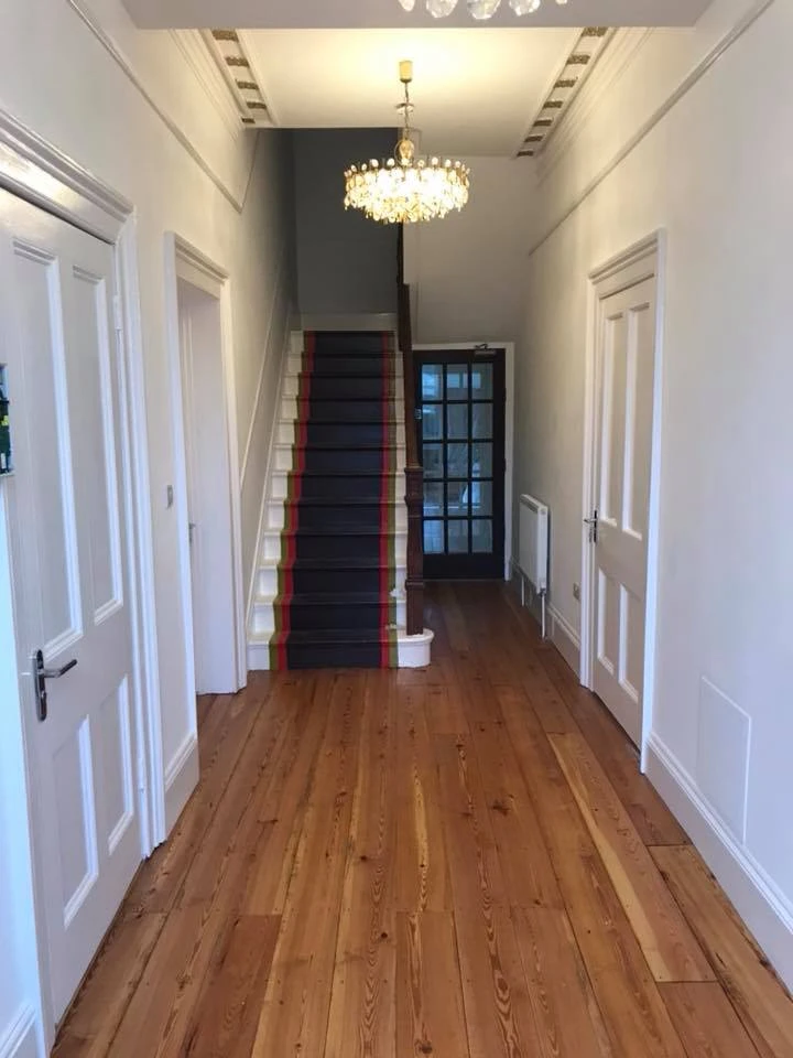 Elegant hallway with white walls, wooden flooring, and staircase with striped runner