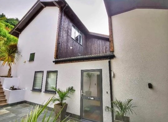 The Fernery exterior showing white walls with dark wooden cladding and potted plants