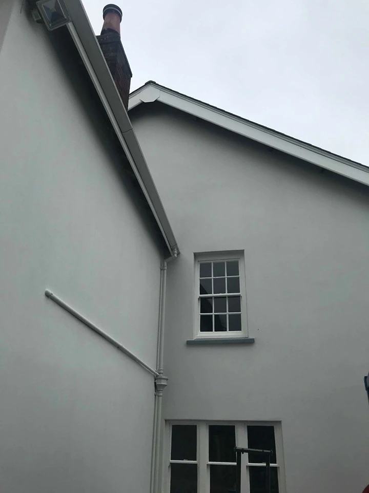 White house exterior with window and downpipe, showing roof detail