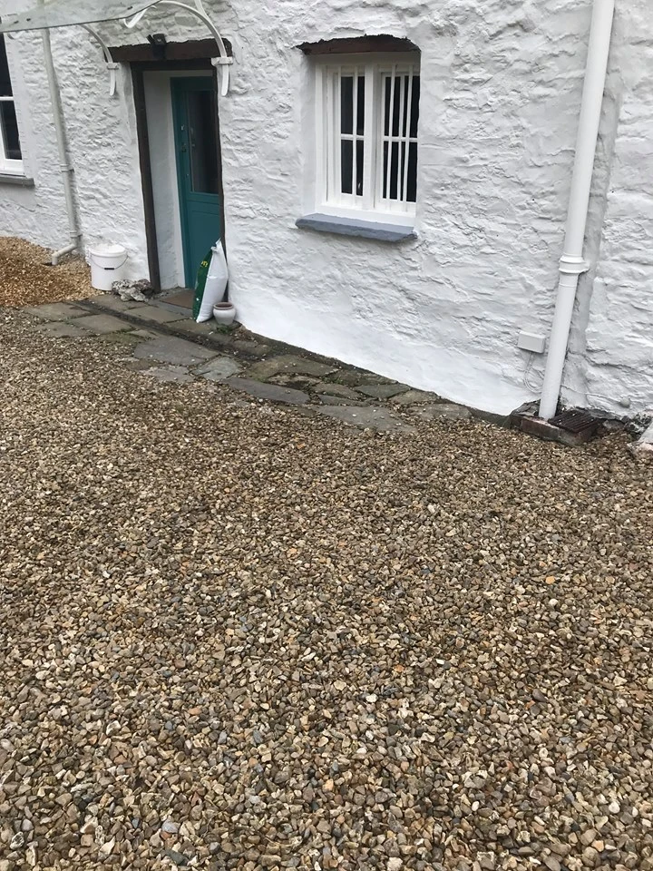 White textured cottage exterior with teal door, window and gravel driveway