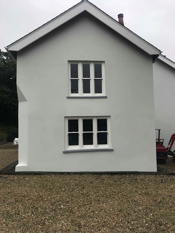 White rendered house with gray windowsills and gravel driveway