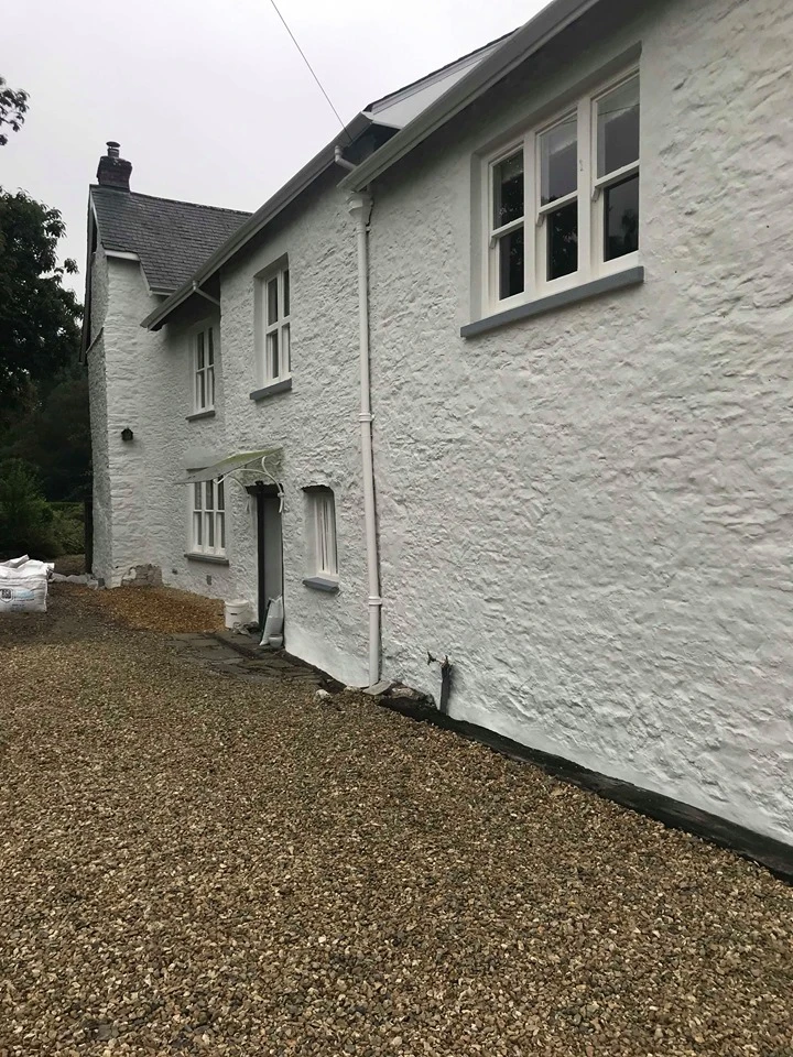 White textured house exterior with multiple windows and gravel driveway