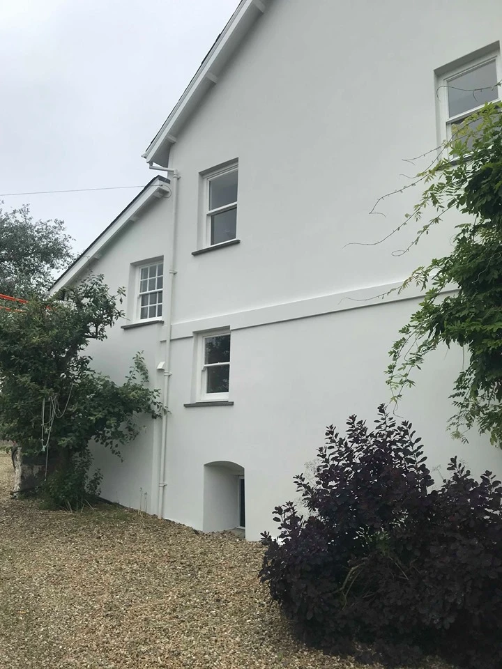 White painted house exterior with multiple windows and surrounding vegetation on gravel driveway