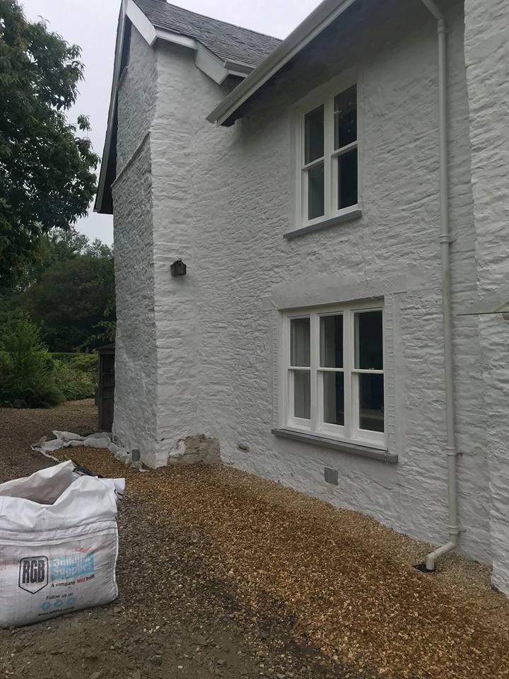 White textured house exterior with windows and gravel ground, showing corner view